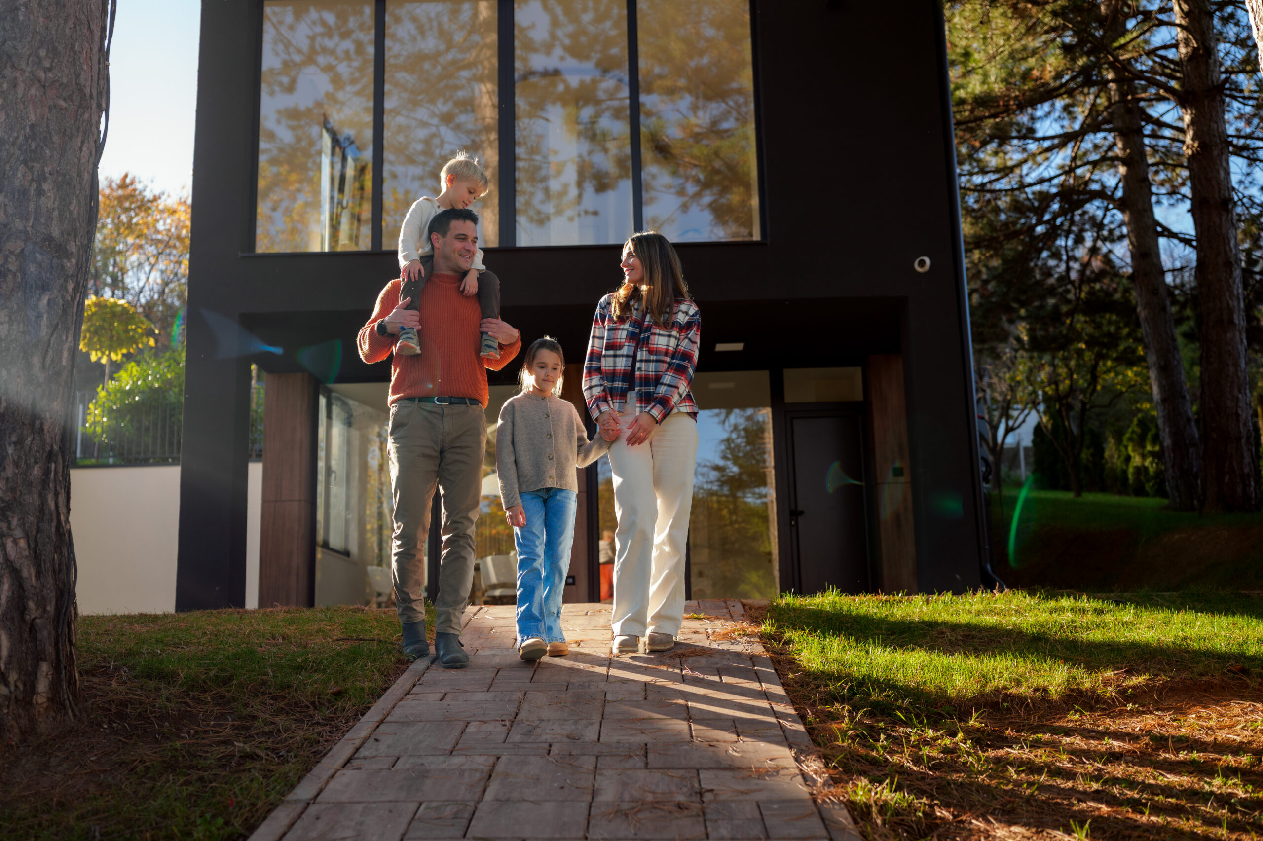 Familie mit zwei Kindern auf dem Weg vor einem modernen Einfamilienhaus im Herbst
