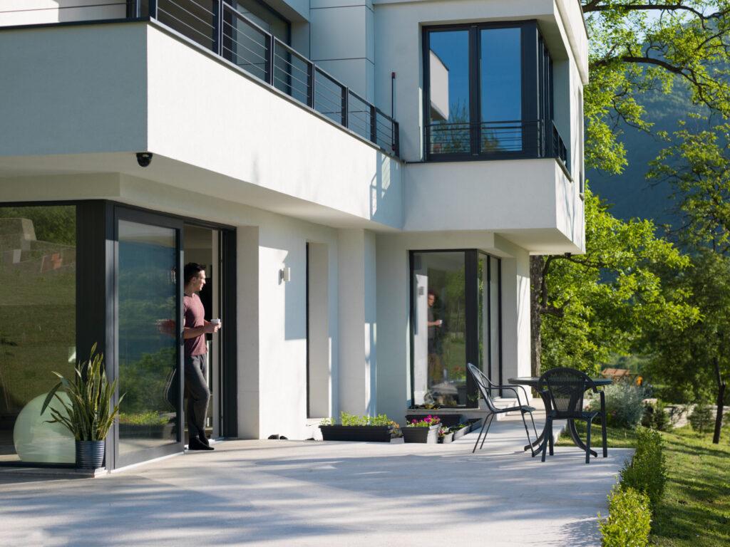 Mann mit Kaffeetasse vor einer modernen Villa mit großen Glasfronten